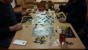 Bild: Spielmaterial auf Tisch mit zwei gegnerischen Spielern