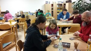 Bild: viele Spieler - Erwachsene und Kinder - sitzen an verschiedenen Tischen beim gemeinsamen Spiel beisammen