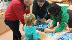 Bild: Erwachsene und Kinder stehen um eine Spielschachtel