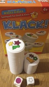 Bild: im Hintergrund Spielschachtel Klack, im Vordergrund gestapelte Spielscheiben und Würfel