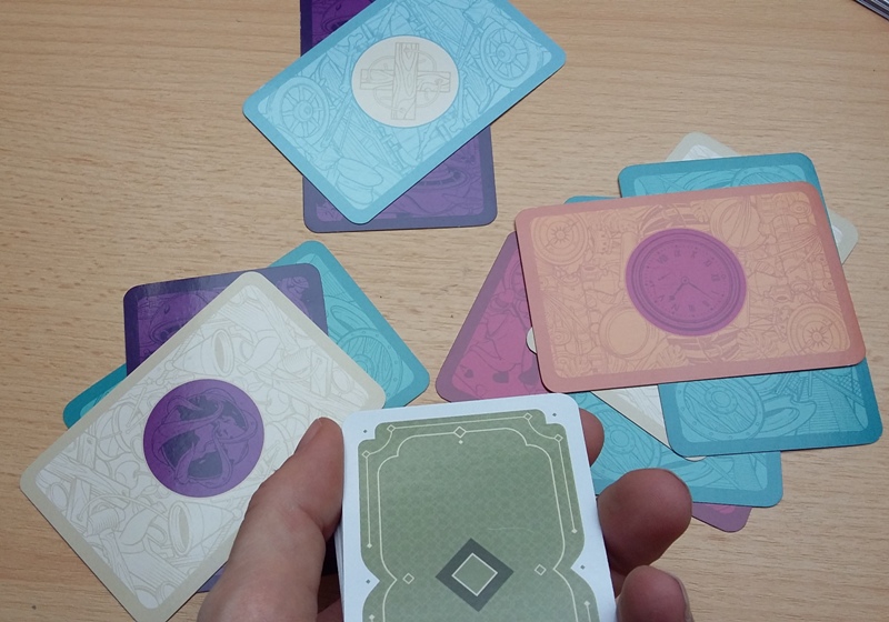 Bild: verdeckter Kartenstapel in der Hand eines Spielers, auf dem Tisch liegen mehrere zweifarbige Spielkarten