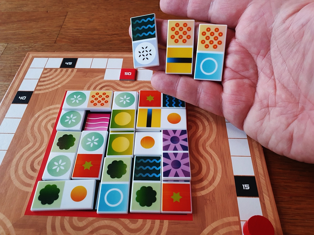 Eine Hand mit drei Spielsteinen über einem halb gefüllten Spielbrett