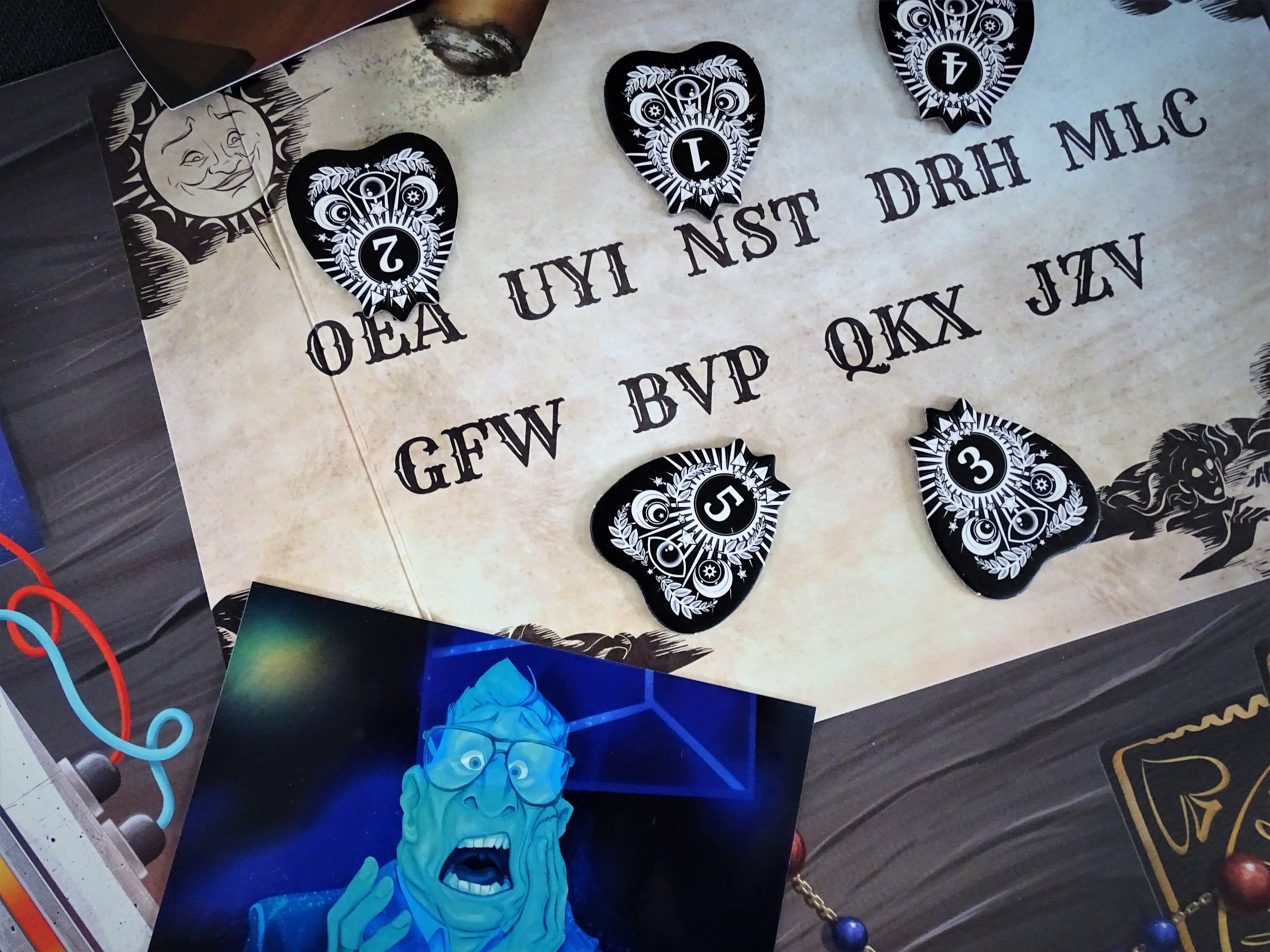 Ein Blick auf das Ouija-Brett zeigt fünf Marker, die auf Buchstaben deuten. 
