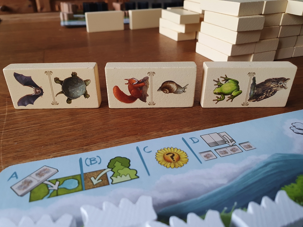 Drei Dominosteine mit Tierabbildungen vor dem Spielertableau