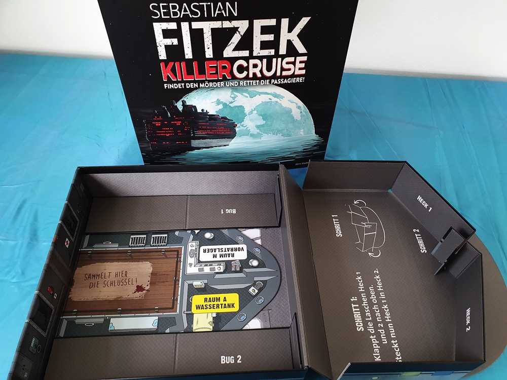 Im Boden des Spielkartons befinden sich zusammengefaltet Bug und Heck des Schiffes. Eine Seite ist ausgeklappt und zusammengesteckt.