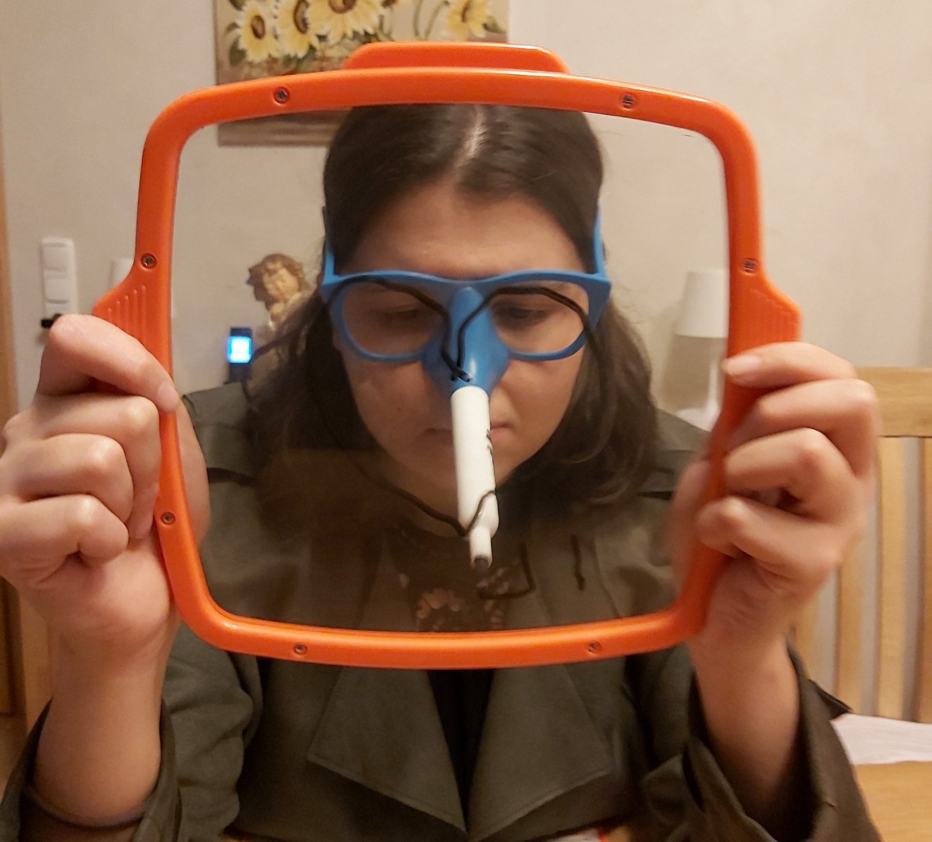 Zu sehen ist eine Frau, die mithilfe einer Zeichenbrille und ihrer Nase ein Herz auf ein transparentes Zeichenbrett malt.