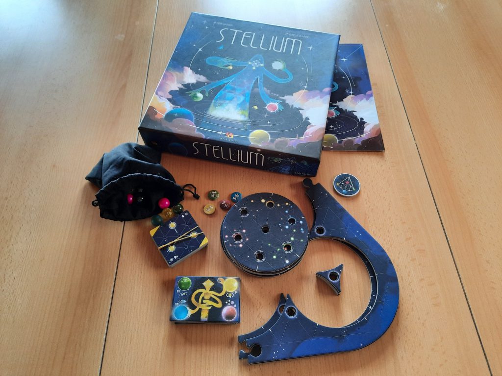 Spielekarton und Beschreibung, ein Beutel mit Murmeln, ein Stapel Aufgabenkarten, ein Spielhilfeplättchen, mehrere Kreise übereinander mit Löchern für das Spielbrett, die restlichen Spielbrettteile, ein rundes Startspielerplättchen