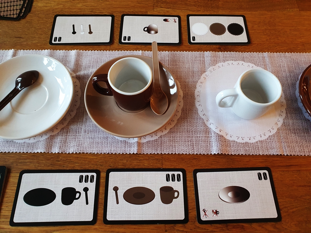 In der Tischmitte zwei Untertassen in weiß und braun, darauf eine oder keine Tasse, dazu ein oder kein Löffel.