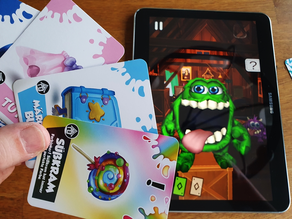 Das animierte Monster in der App mit geöffnetem Maul, daneben Kartenhand
