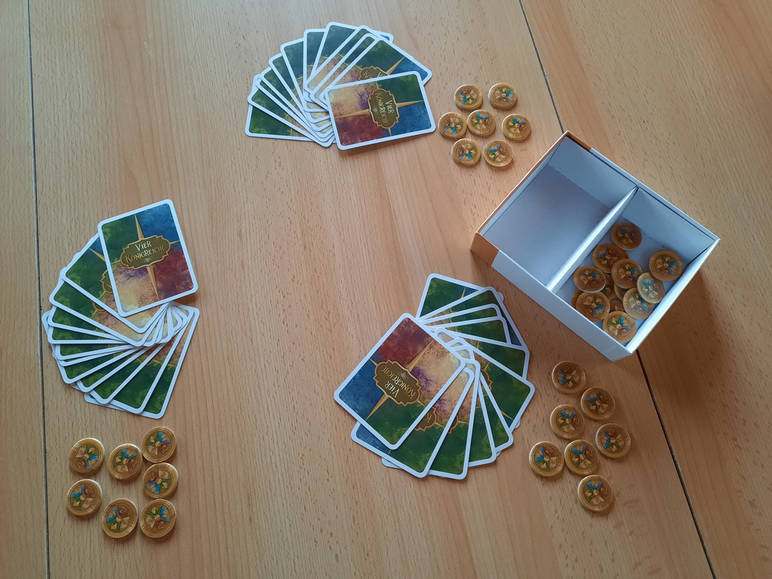 Es liegen Spielkarten (3 Stapel mit je 12 Karten) und Münzen auf dem Tisch. Ausserdem steht die Spielpackung mit den restlichen Münzen auf dem Tisch.