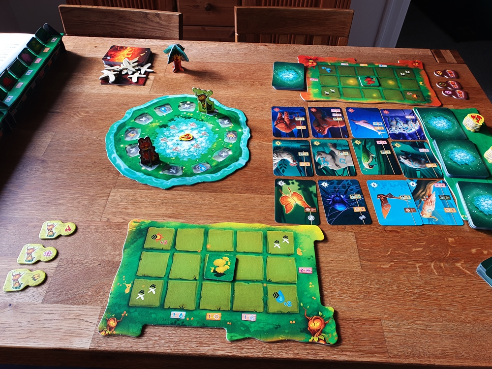 Spielaufbau für zwei Personen; Kartenauslage von 12 Karten, jeweils eigener Spielplan für die Spielenden, Spielbrett Steinkreis mit Figuren