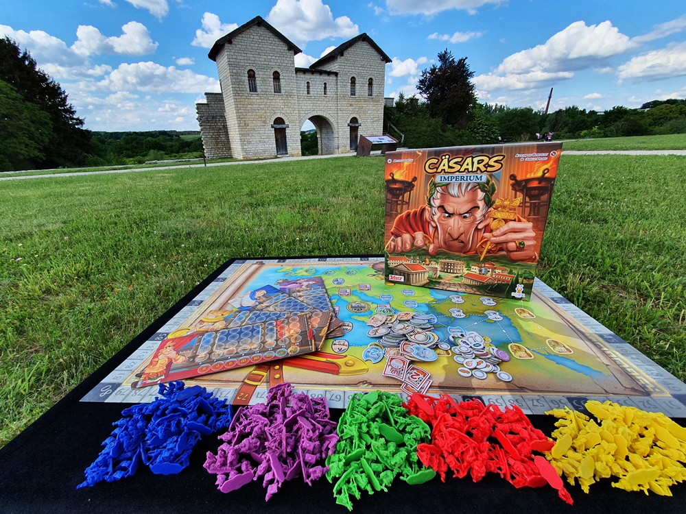 Spielkarton und Inhalt auf einer Wiese vor einem Römertor