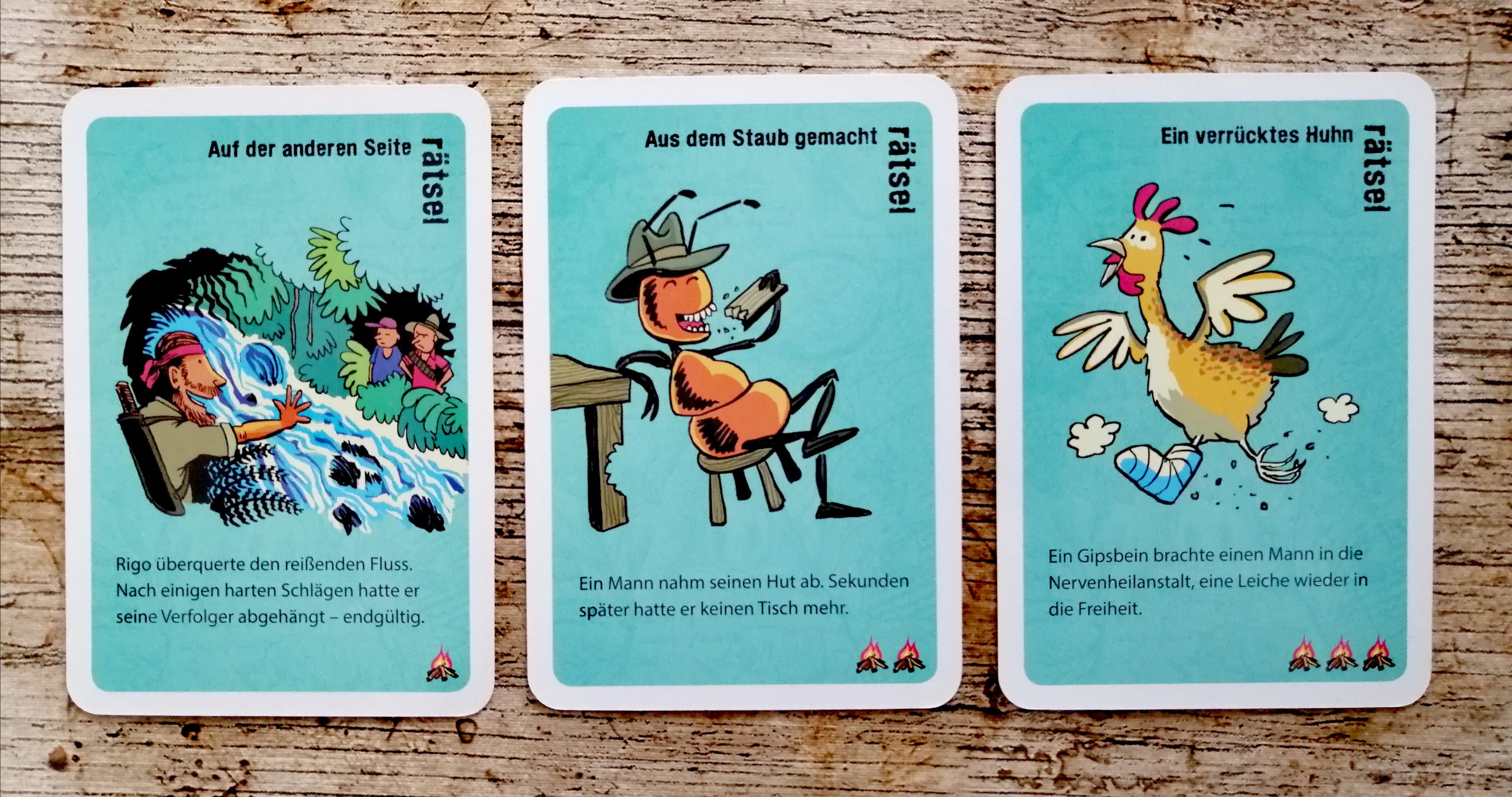 Insgesamt gibt es drei Schwierigkeitsstufen. Diese sind durch Lagerfeuerzeichen unten rechts erkennbar. Alle Karten haben einen türkisen Hintergrund. Darauf ist ein kurzer Text mit einer ansprechenden Zeichnung zu sehen.