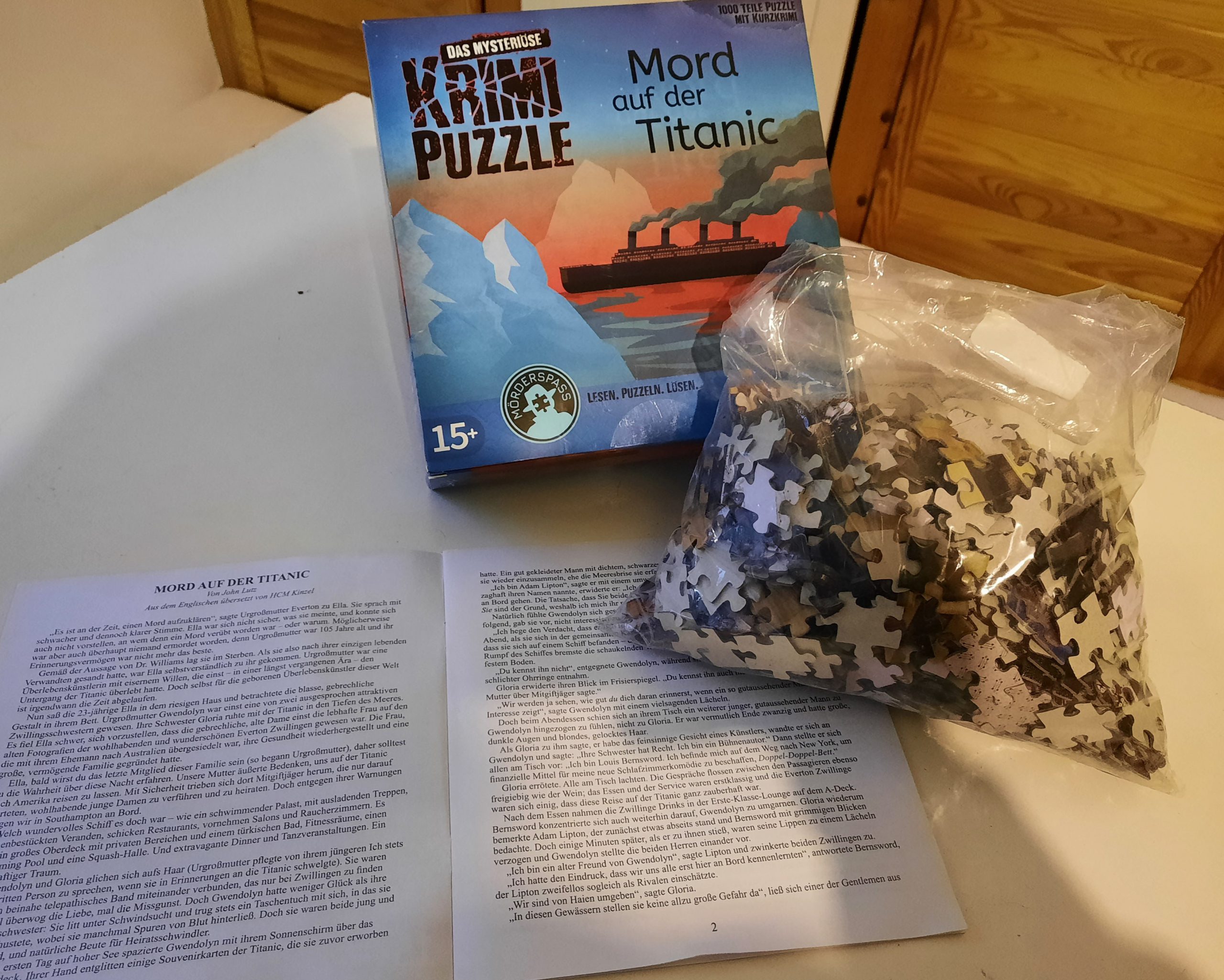 Die Verpackung und ein Beutel mit vielen Puzzleteilen liegen auf dem Tisch. Daneben liegt das Begleitheft aufgeschlagen.
