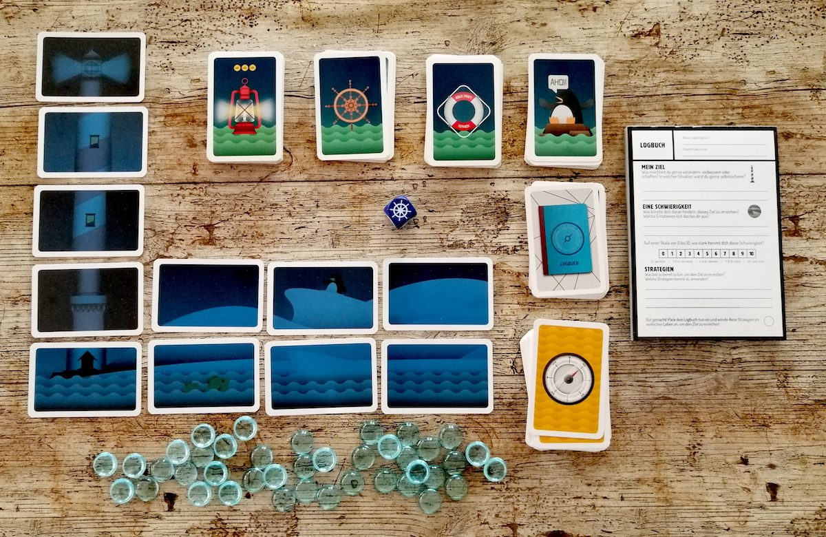 Spielaufbau. Die Karten werden zu einem Leuchturm mit Meer aufgebaut. Die Aktionskarten werden ebenfalls bereitgelegt. 