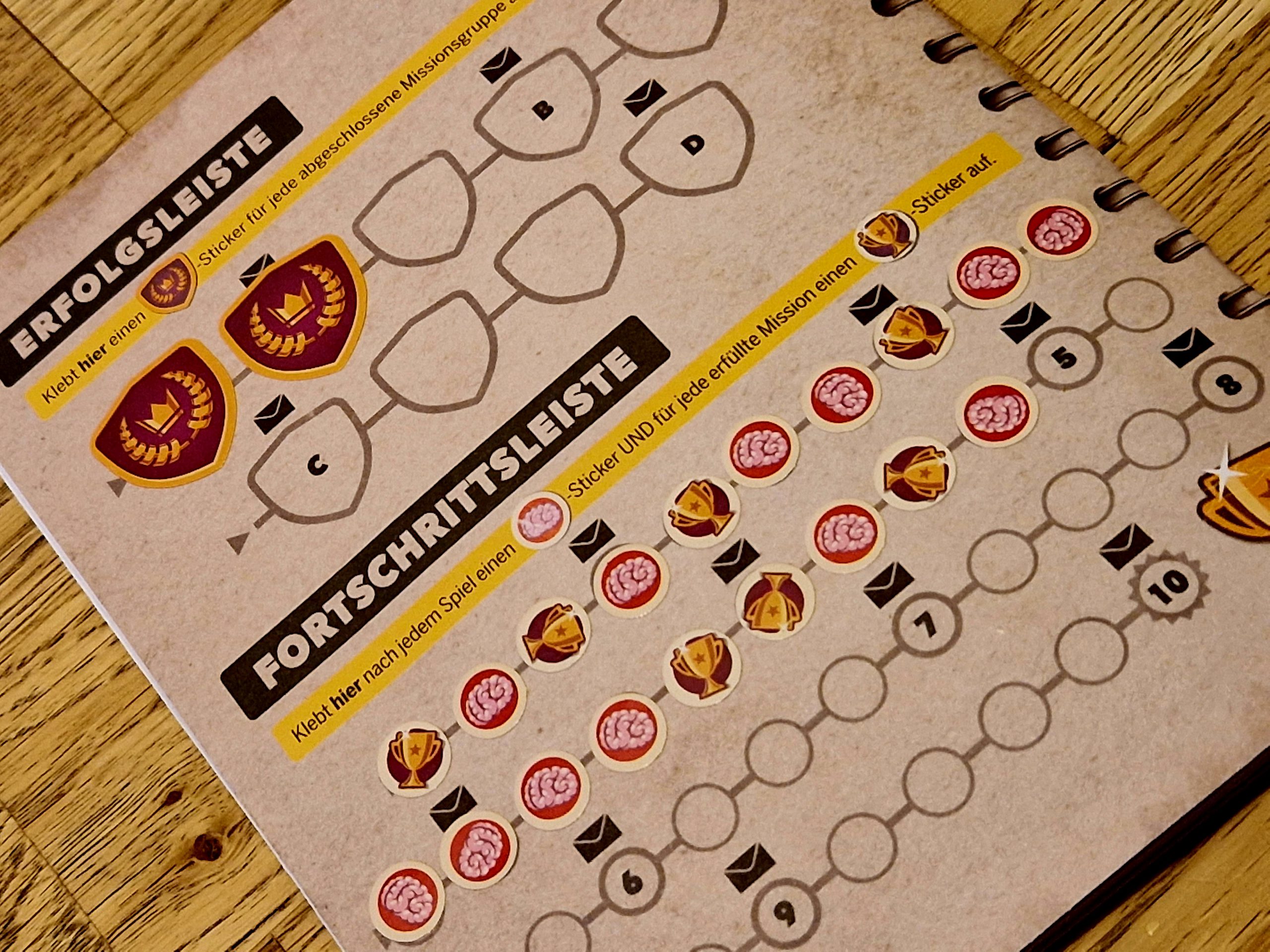 Bild vom Heft und der Leiste, auf die Sticker geklebt werden und die neue Umschläge frei schalten.