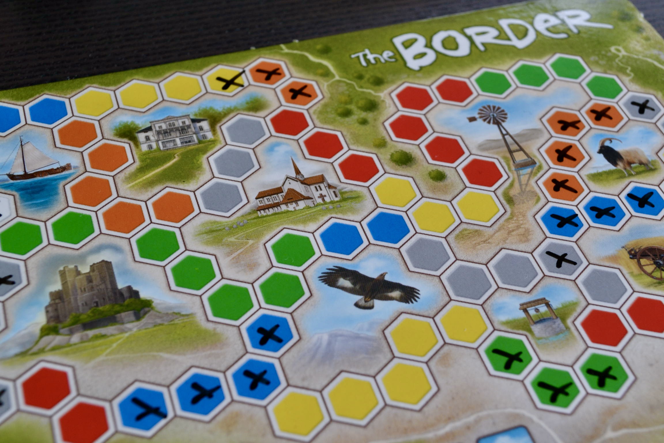 Eine Nahaufnahme des Spieltableaus mit den verschiedenen Gebieten, die mit farbigen Hexagonfelder umkreist sind (die Kirche, die Burg, das Windrad, der Falke, das Boot).