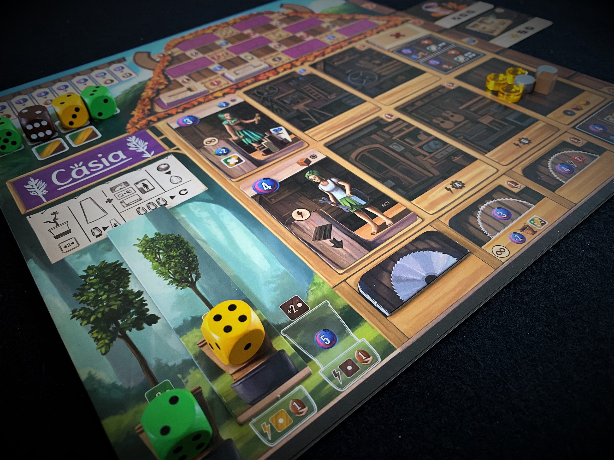 Würfel liegen im Vordergrund. Das Spielboard zeigt die Werkstatt.