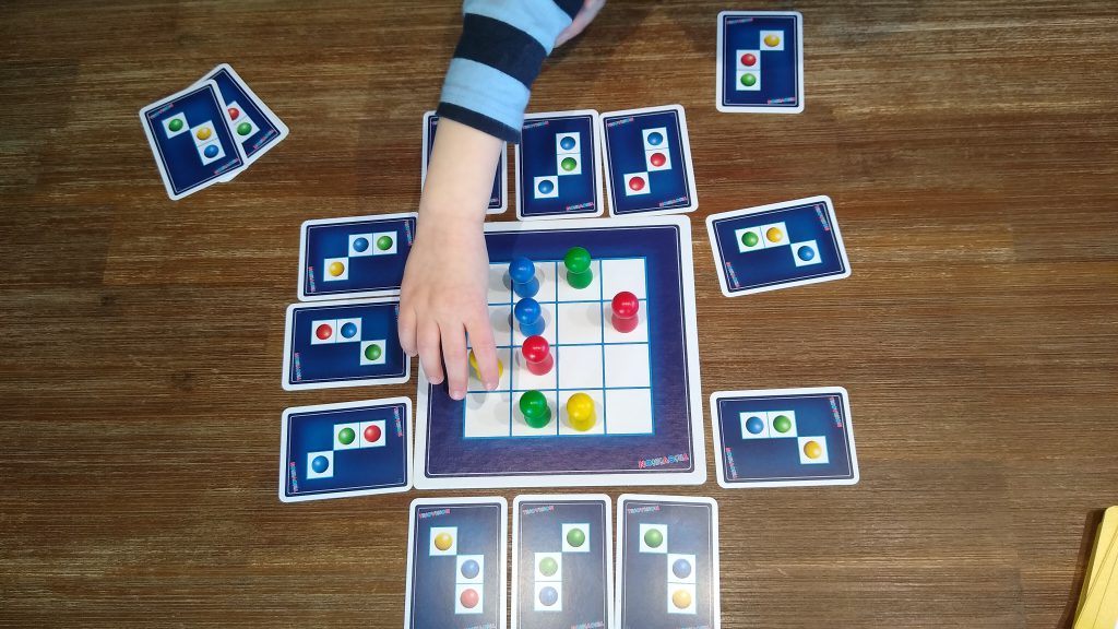 Der Spielplan, ausliegende Karten. Eine Hand greift zu einer Spielfigur