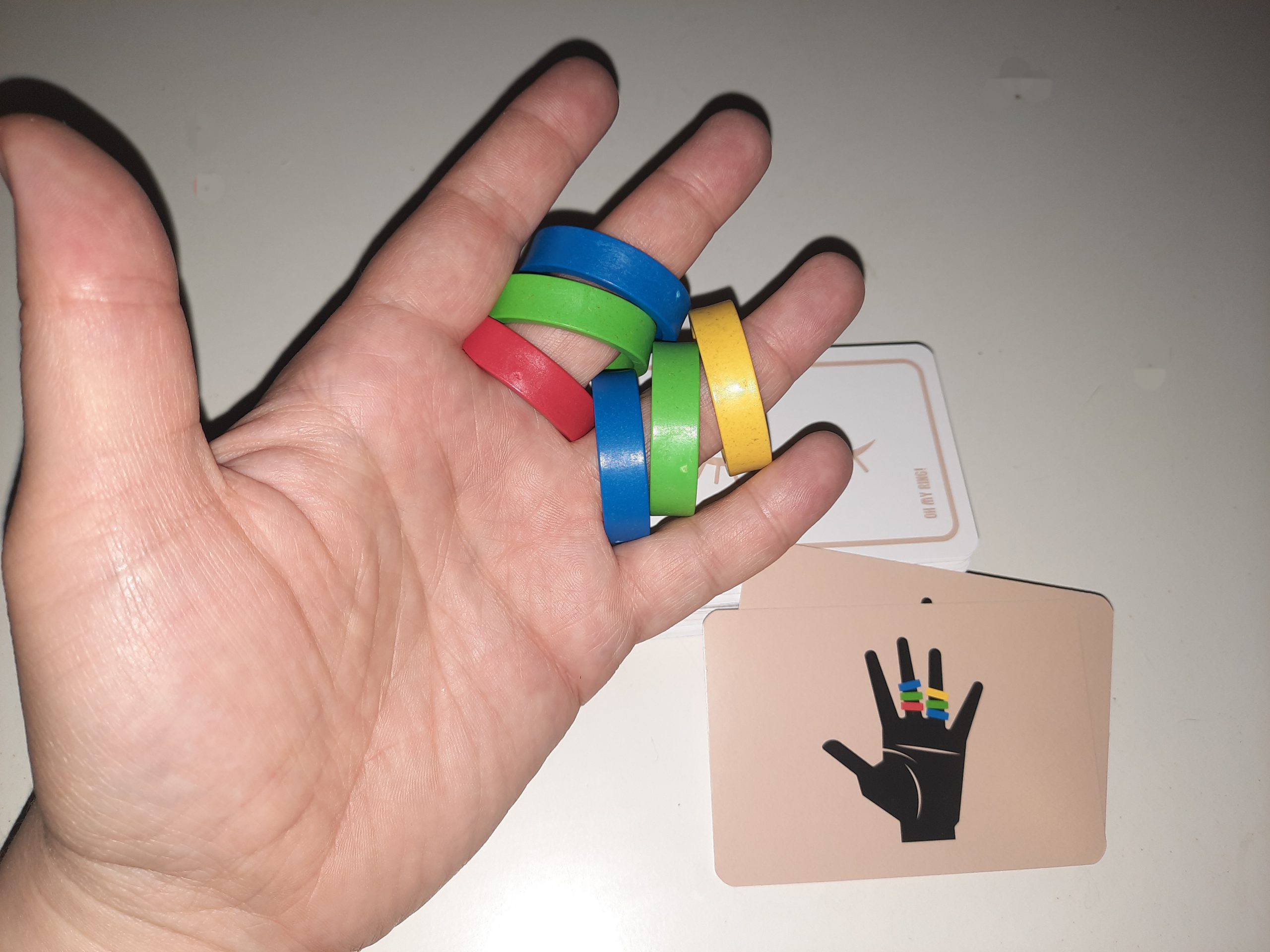 Zu sehen sind eine Hand mit sechs bunten Ringen und eine Aufgabenkarte.