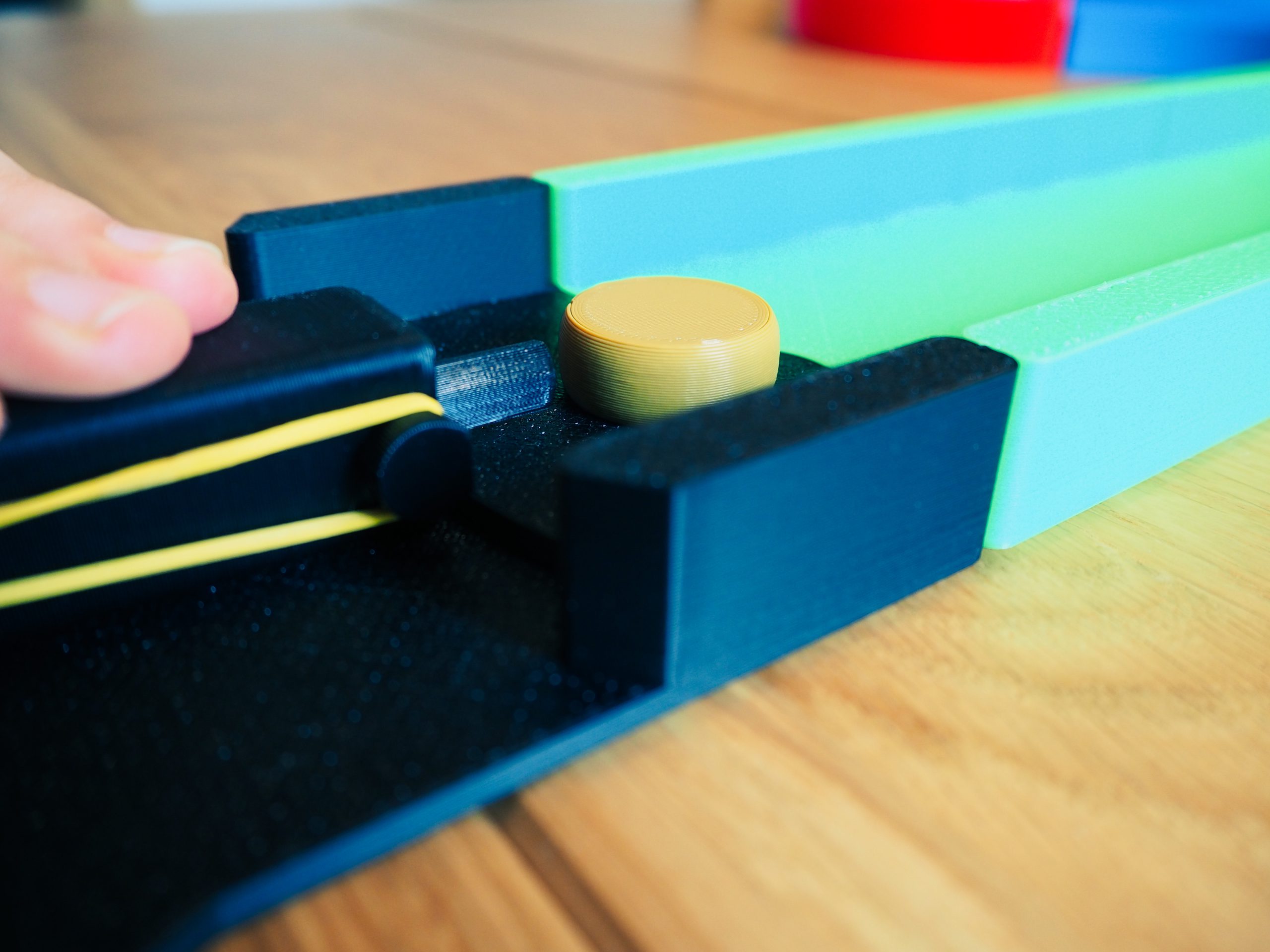 Auf dem Bild ist eine Nahaufnahme der Spielsteineschnipser zu sehen. Er wird von zwei Fingern gehalten und davor liegt ein Spielstein, der bereit ist losgeschossen zu werden.