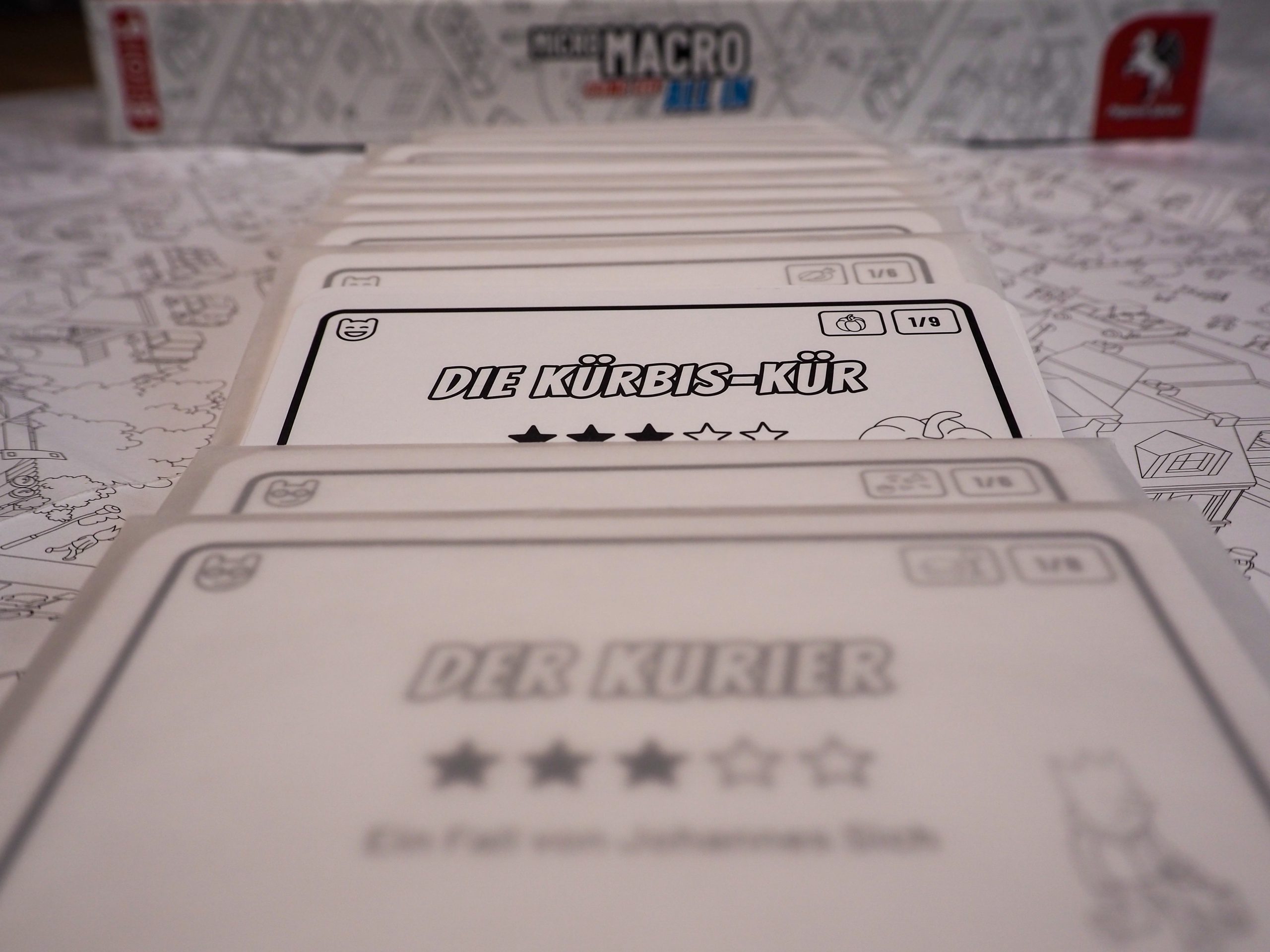 Im Hintergrund ist unscharf die Spielschachtel zu sehen. Im Vordergrund sind die Fälle hintereinander aufgereiht und ein Fall, etwa in der Mitte des Bilds ist fokussiert. Er trägt den Namen "Die Kürbis-Kür".