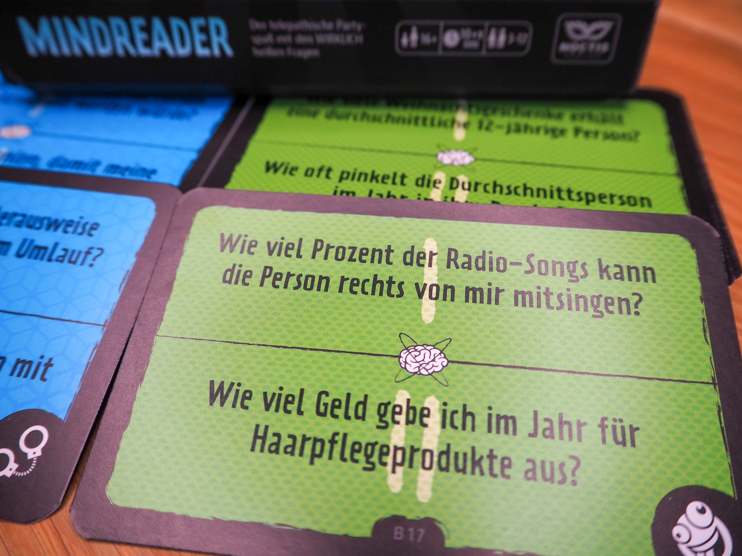 Im Hintergrund ist verschwommen die Spielschachtel zu sehen, während im Vordergrund eine grüne Karte im Fokus liegt.