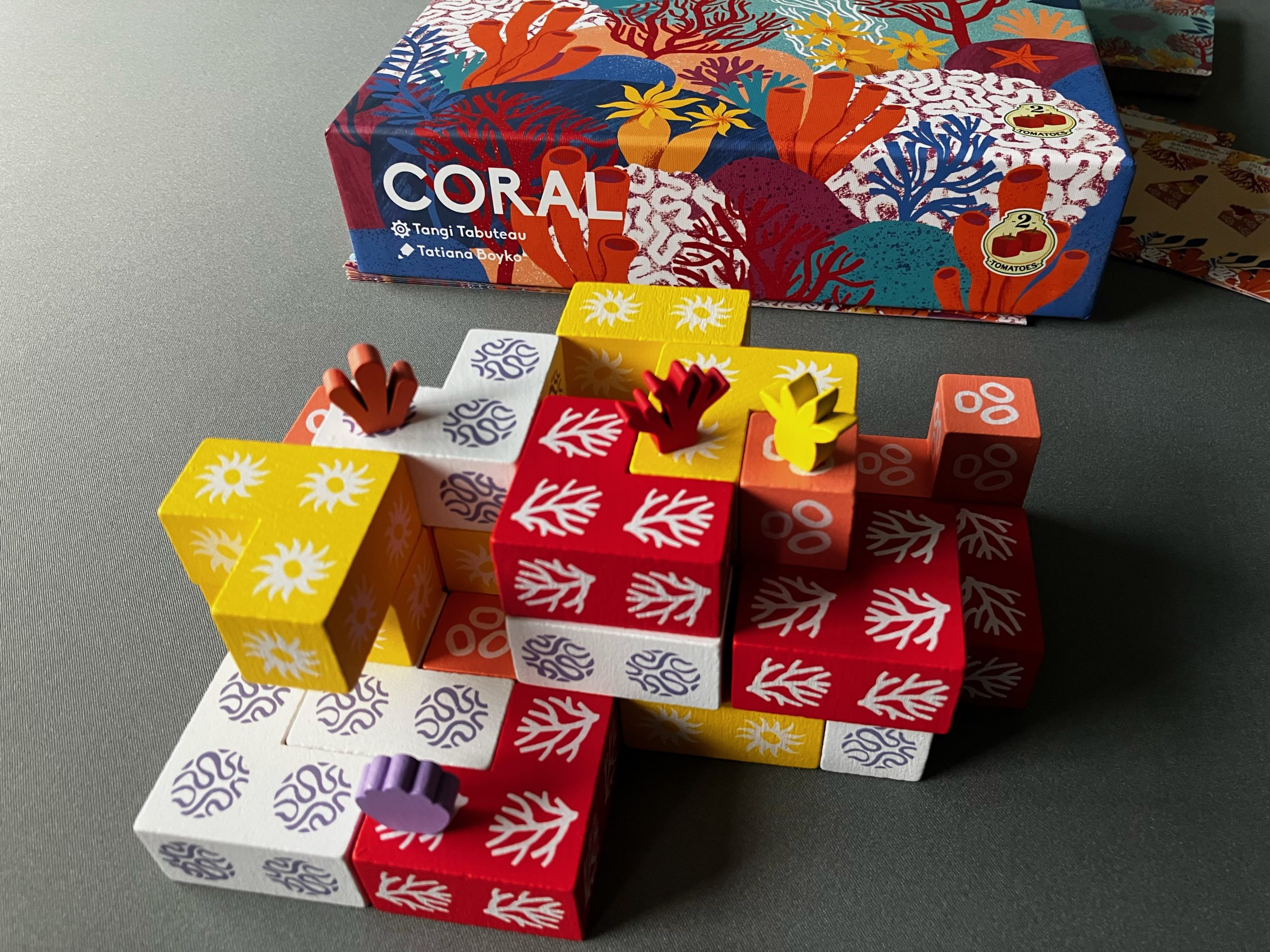 Bunte Korallenspielsteine aus Holz gestapelt mit kleinen Korallenfiguren zeigen eine typische Spielszene.