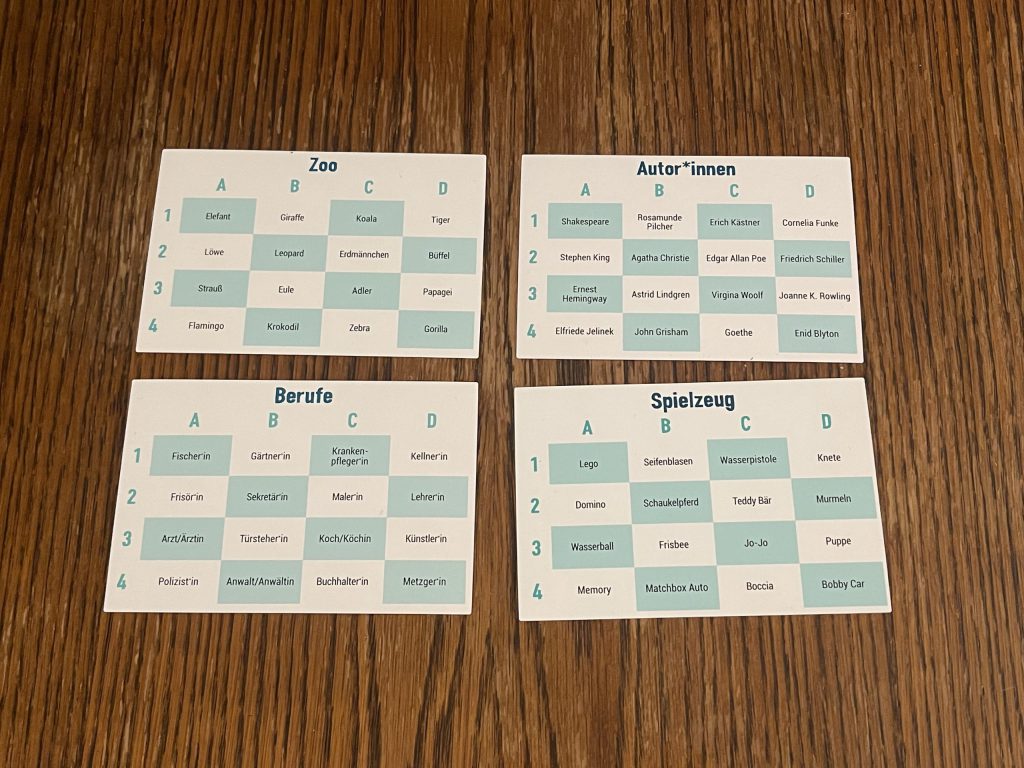 Auf dem Bild befinden sich vier Themenkarten: Zoo, Autor*innen, Berufe und Spielzeug. Auf jeder Themenkarte sind 16 Begriffe dargestellt in einem 4x4 Raster. Sodass jedem Begriff ein Buchstabe und eine Zahl zugeordnet ist.