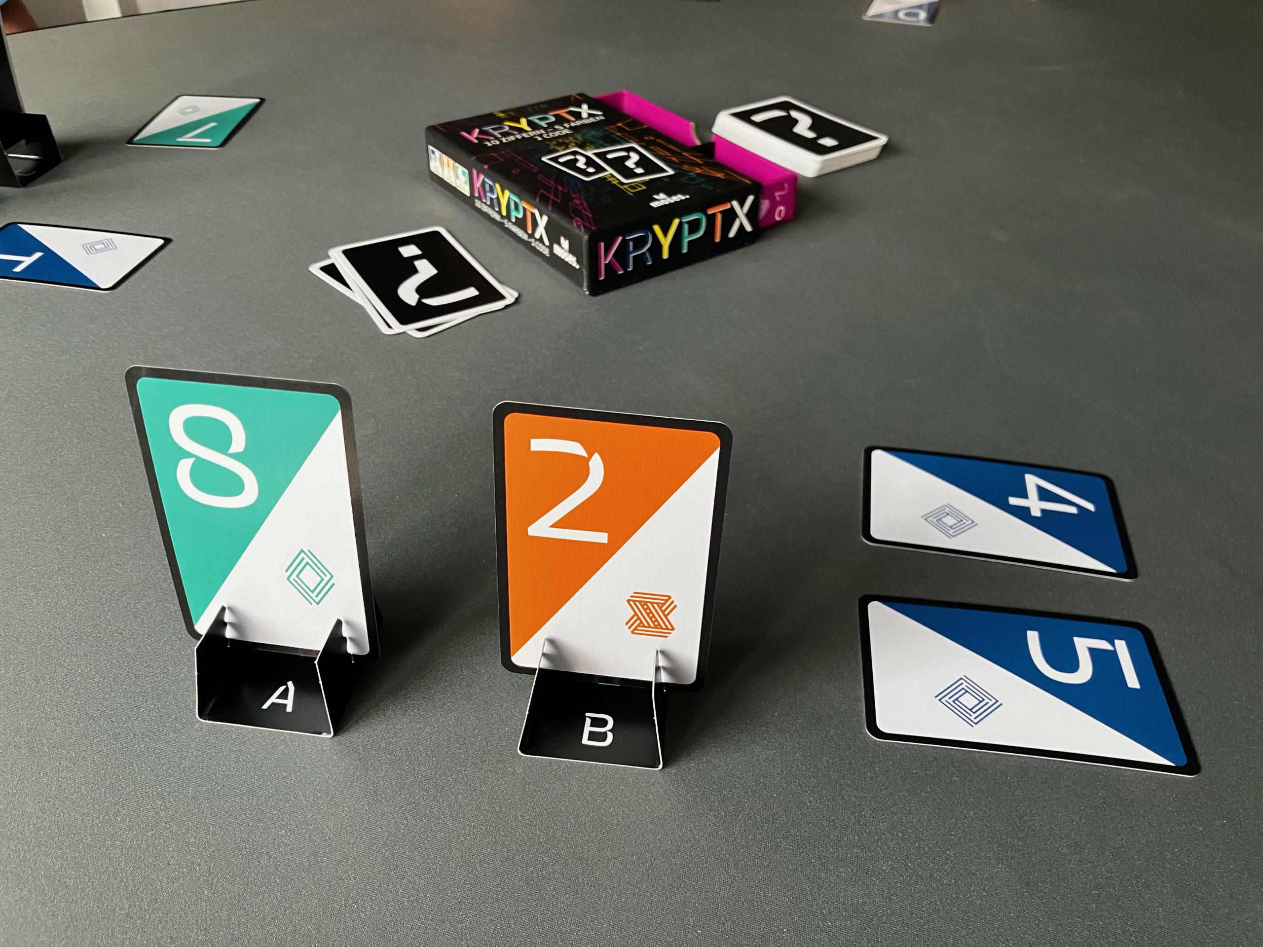 Zwei Karten stehen aufrecht und zeigen den eigenen Code - eine acht und eine zwei. In der Mitte die Spielschachtel.