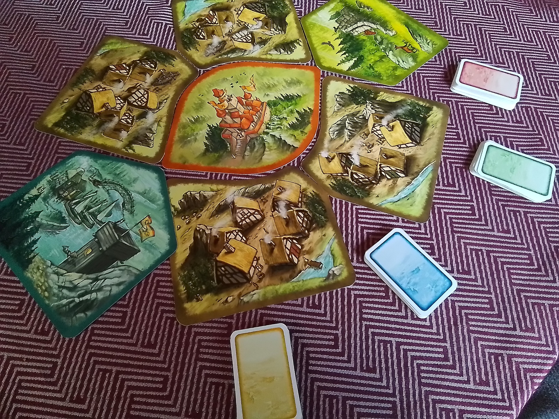 Auf dem Tisch liegen die 7 Elemente/Landschaften des Spielbrettes und 4 Kartenstapel (gelb, blau, grün, rot)