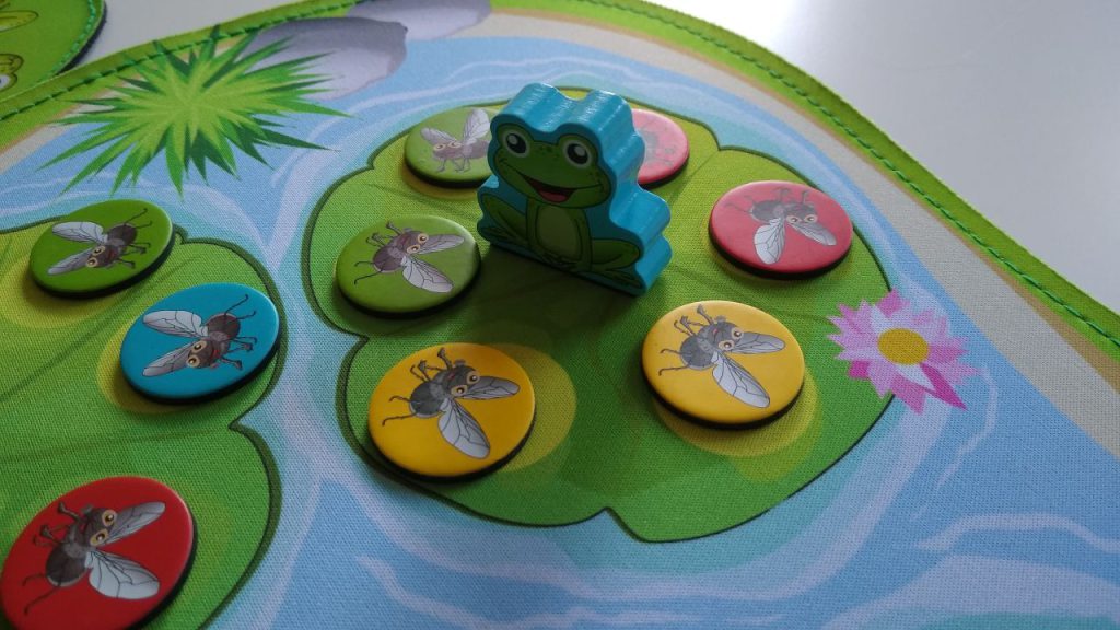 Eine Detailaufnahme einer Froschfigur auf einem noch komplett mit Fliegen-Chips gefüllten Seerosenblatt