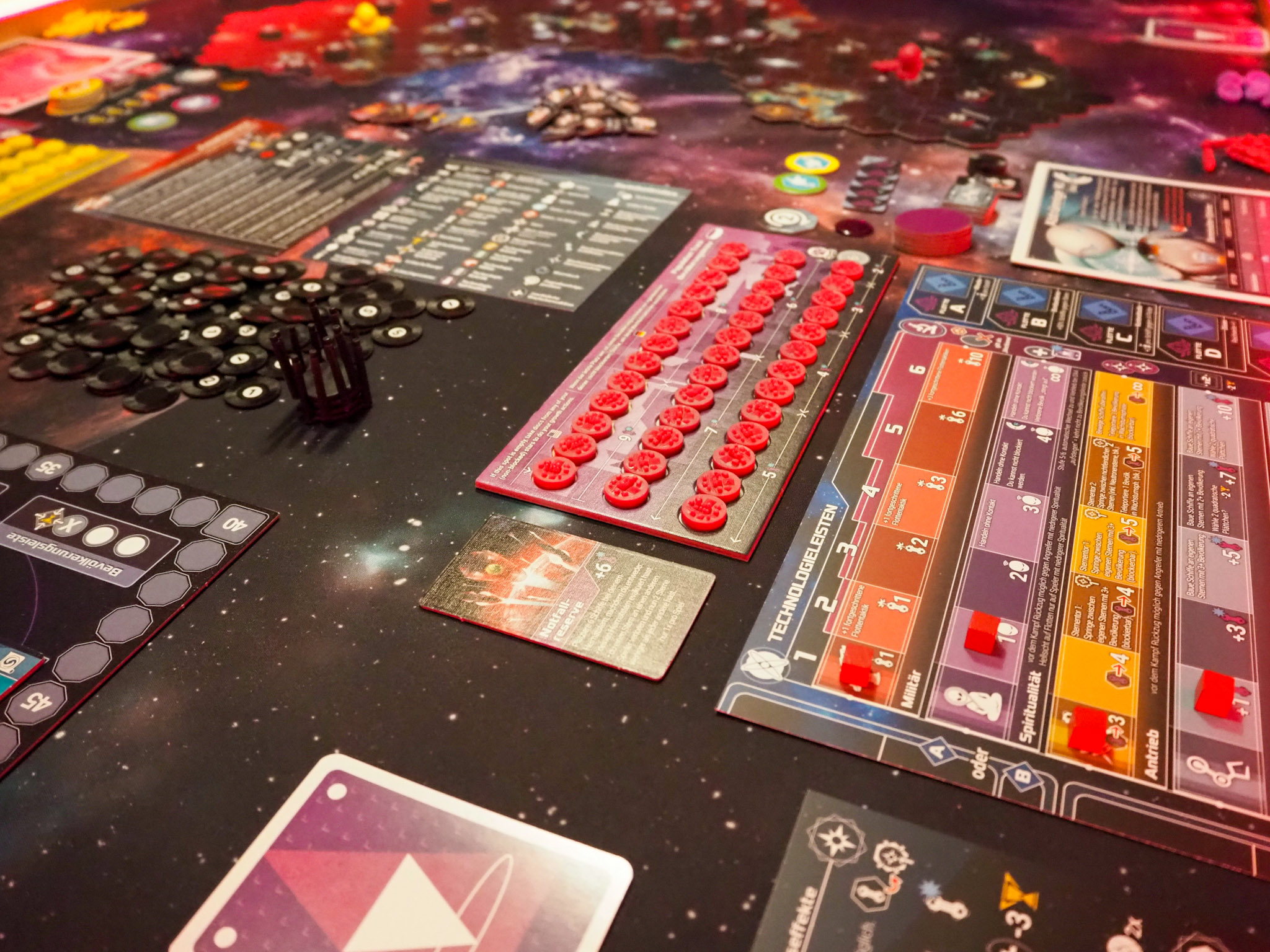 Das Bild zeigt einen Tisch, der mit zahlreichem kleinteiligem Spielmaterial bedeckt ist. Die Farben des Spielmaterials sind lebhaft und bunt.