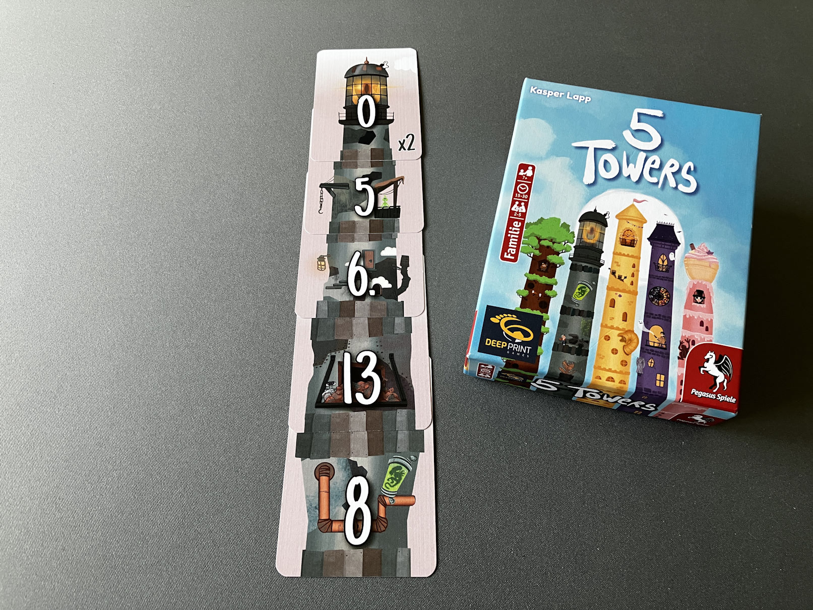 Der graue Turm ist mit 5 Karten aufgestapelt, die Spielschachtel liegt daneben.