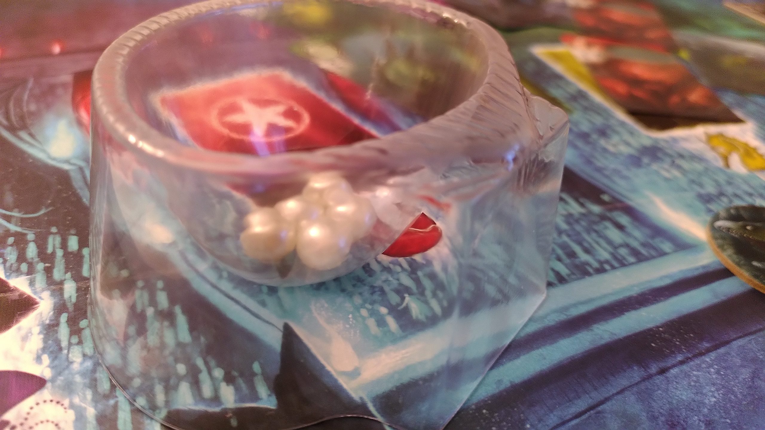 Durchsichtige Plastikschale in Muschelform als Perlenhalter für alle Spielenden. 