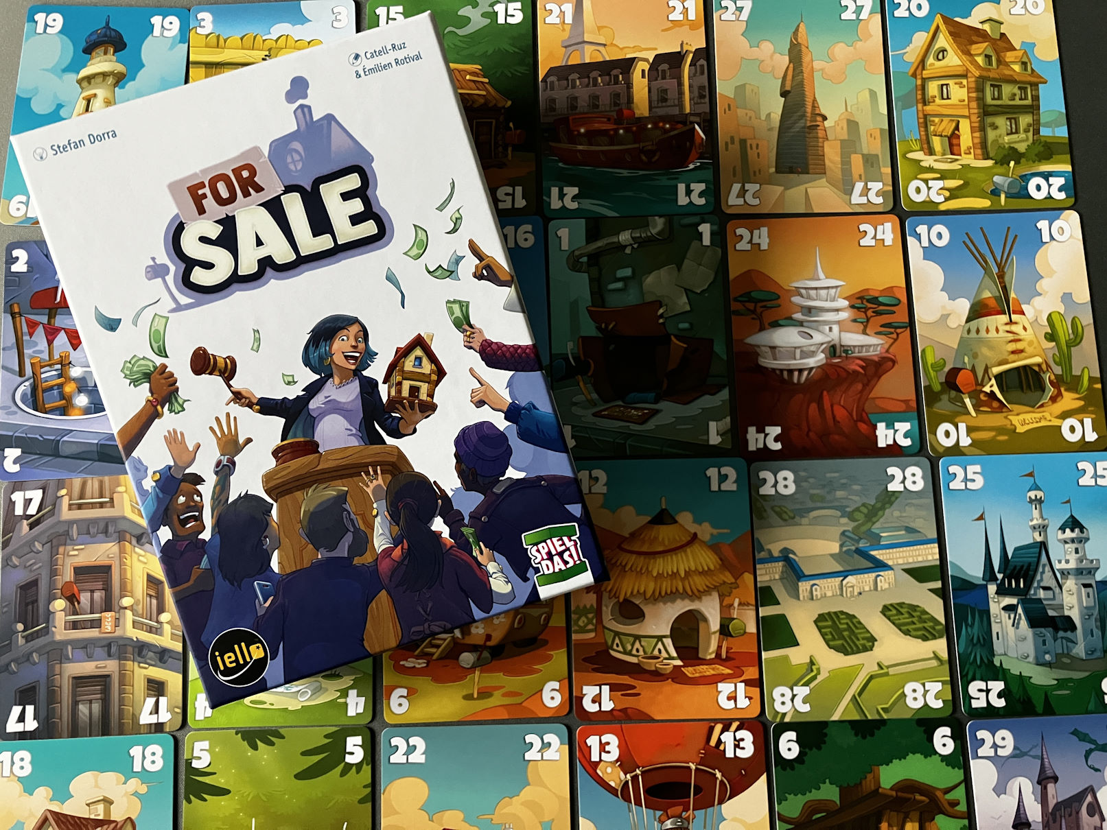 Die kleine Spielschachtel liegt auf den bunten Immobilienkarten drauf.