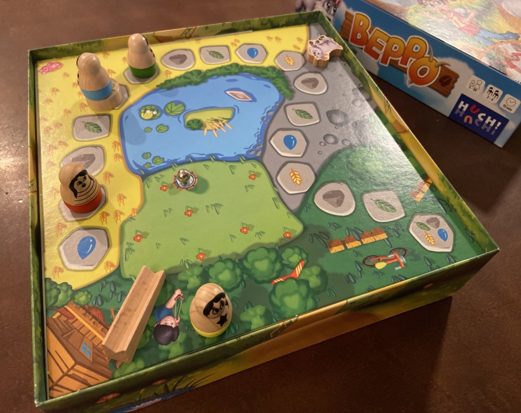 Der aufgebaute Spielplan im Karton mit einer kleinen Holzrampe im Eck