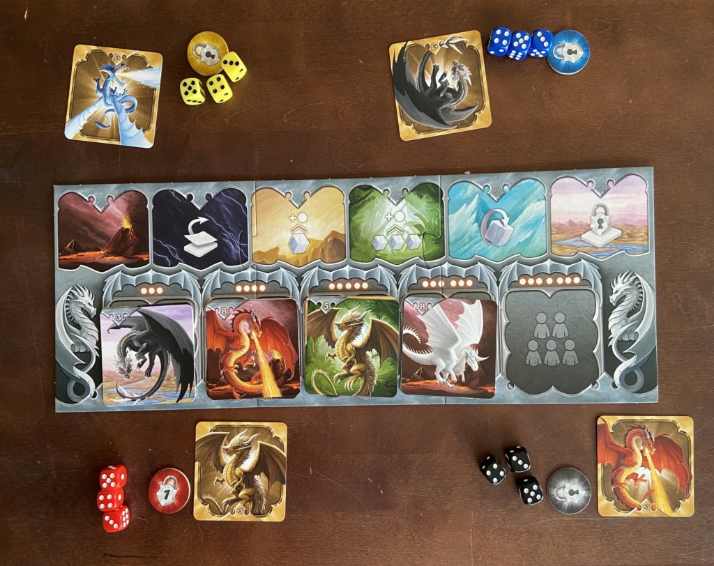 Spielbrett mit ausgelegten Kartenstapeln und jeweils drei gleichfarbige Würfel und eine Drachenkarte drum herum.