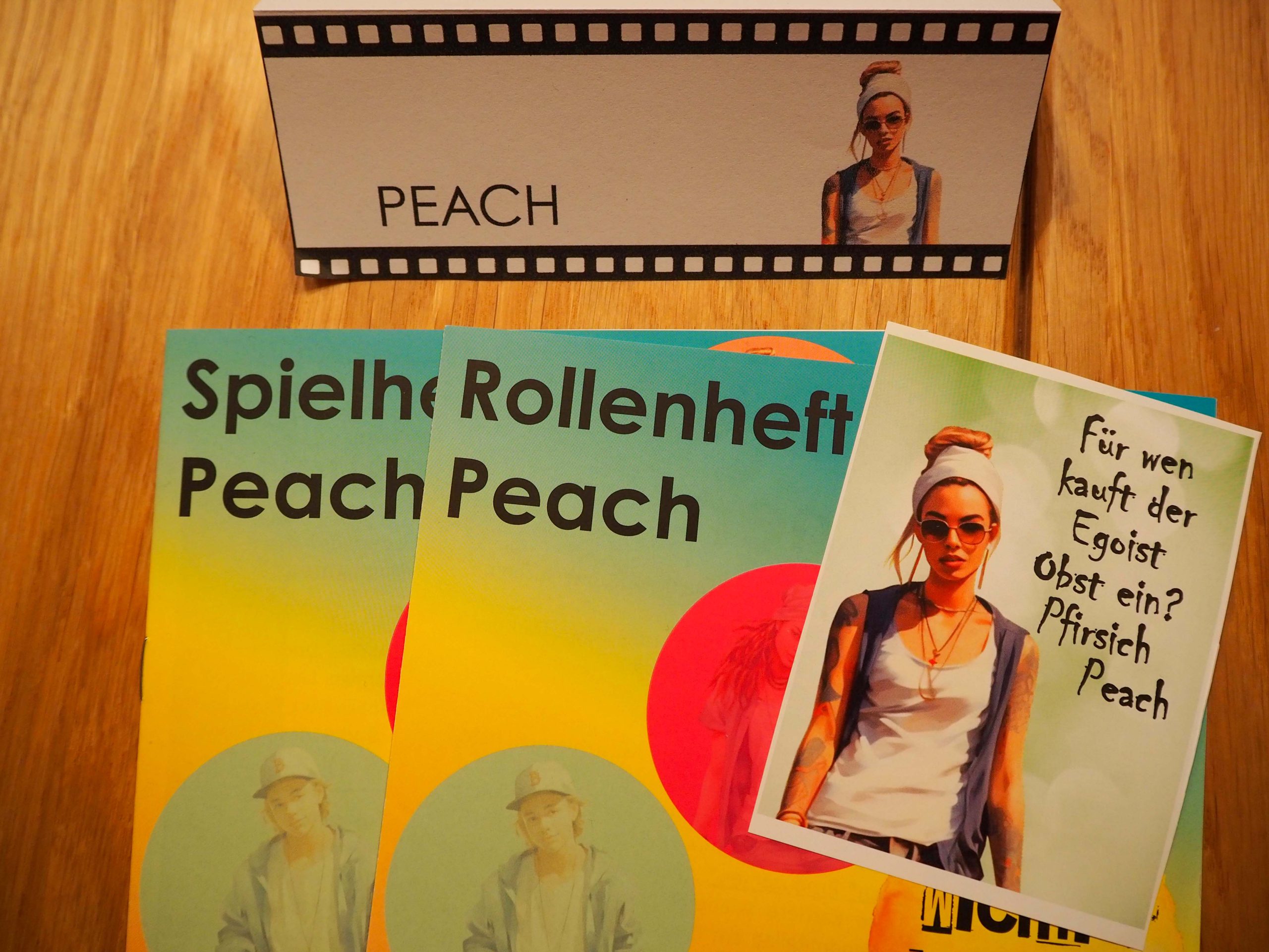Schildaufsteller mit Namen ist wie eine Filmrolle dargestellt. Im Vordergrund Spielheft und Rollenheft in poppigen Farben. Links darüber liegt die Autogrammkarte von Peach. 