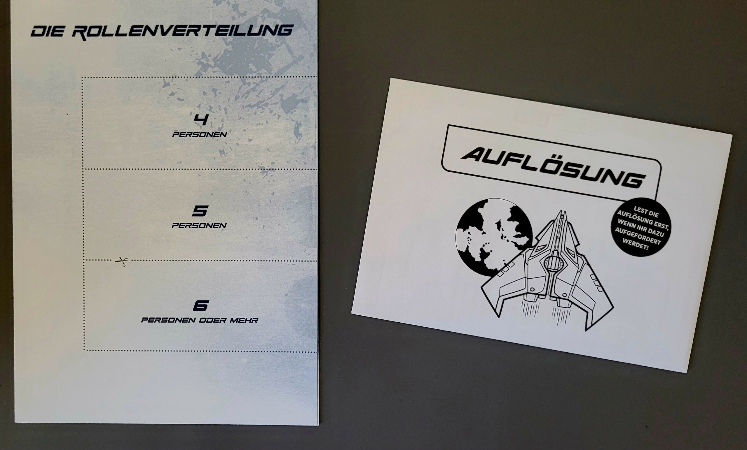 Übersicht zu den Rollenverteilungen und ein Umschlag mit der Auflösung