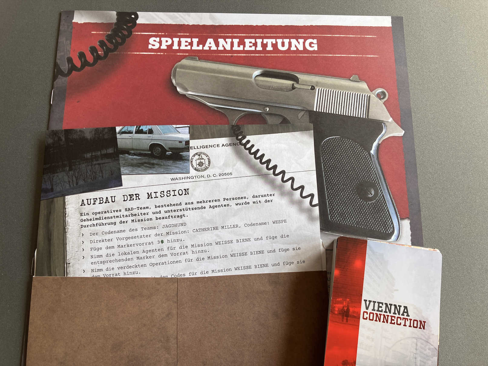 Der Umschlag für Mission 1 liegt geöffnet auf der Spielanleitung