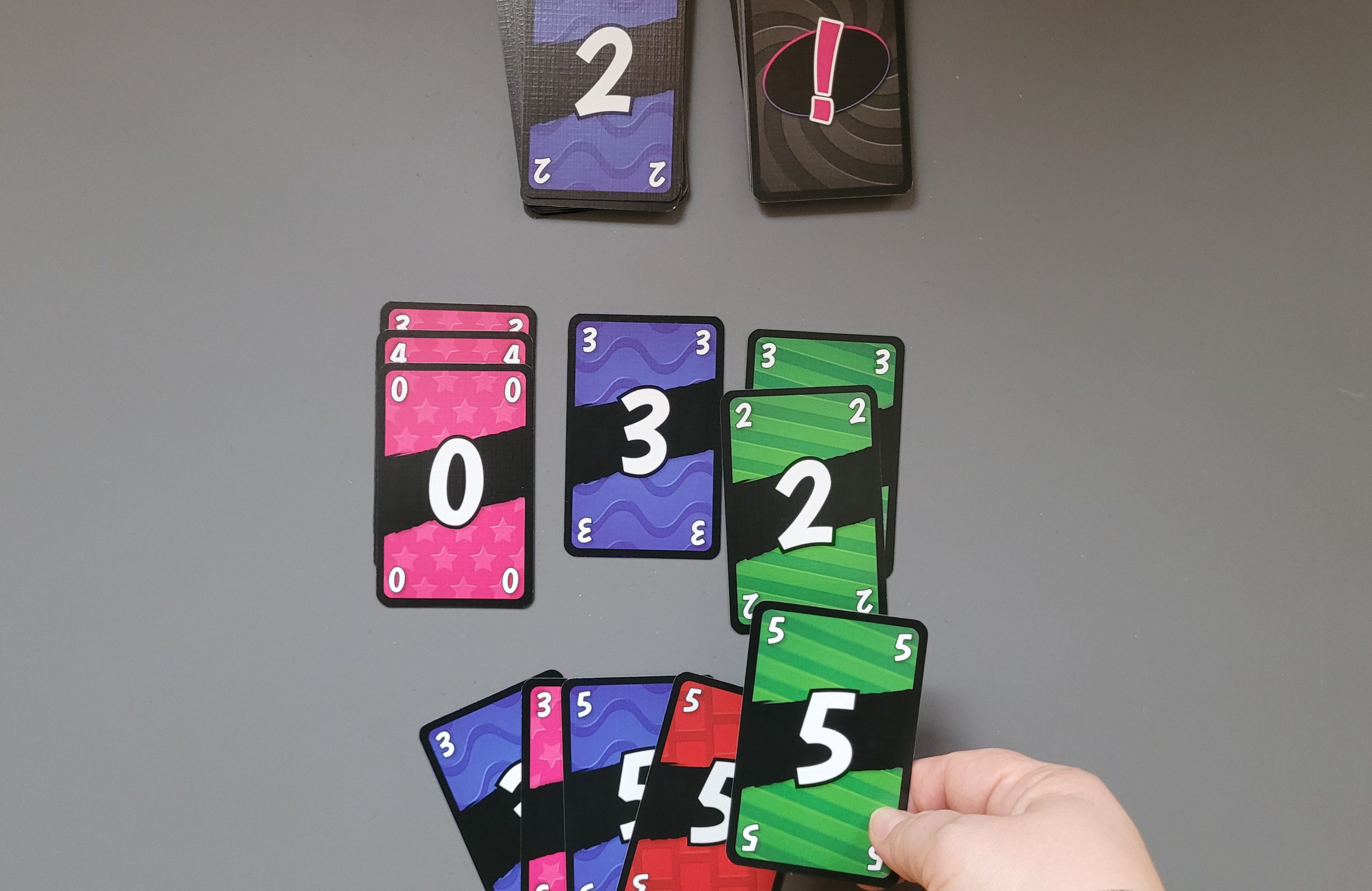 Auf dem Stapel liegt eine blaue 2. Der Spielende will eine grüne 5 als nicht passend legen
