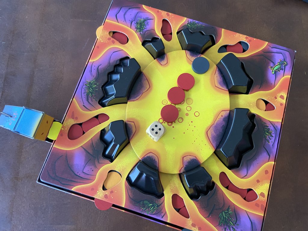 Spielfeld mit Würfel und vier Lavachips auf dem Tableau