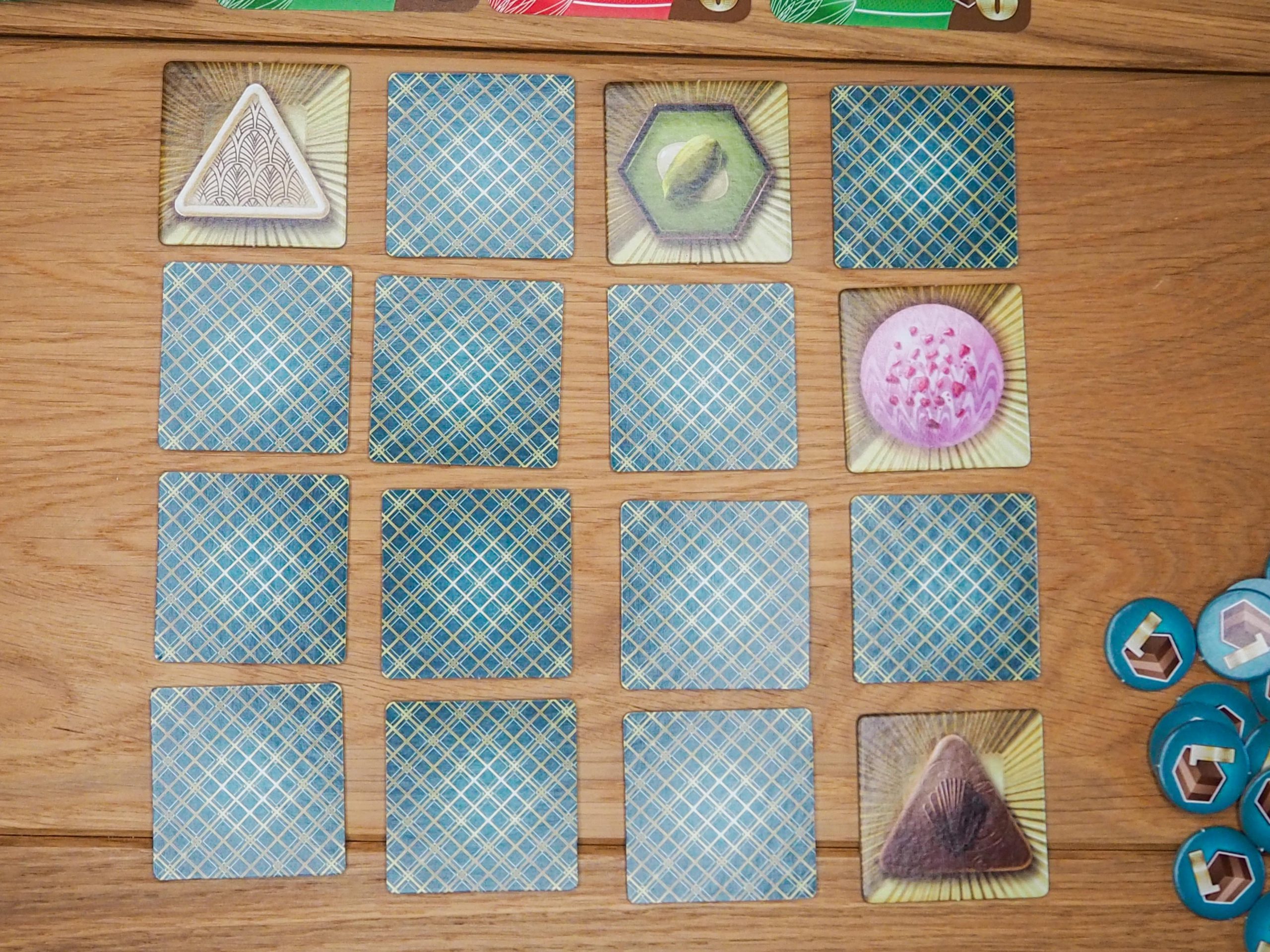 Vier mal vier Raster mit quadratischen Plättchen. Vier davon ausgedeckt. Sie zeigen unterschiedliche Pralinen.