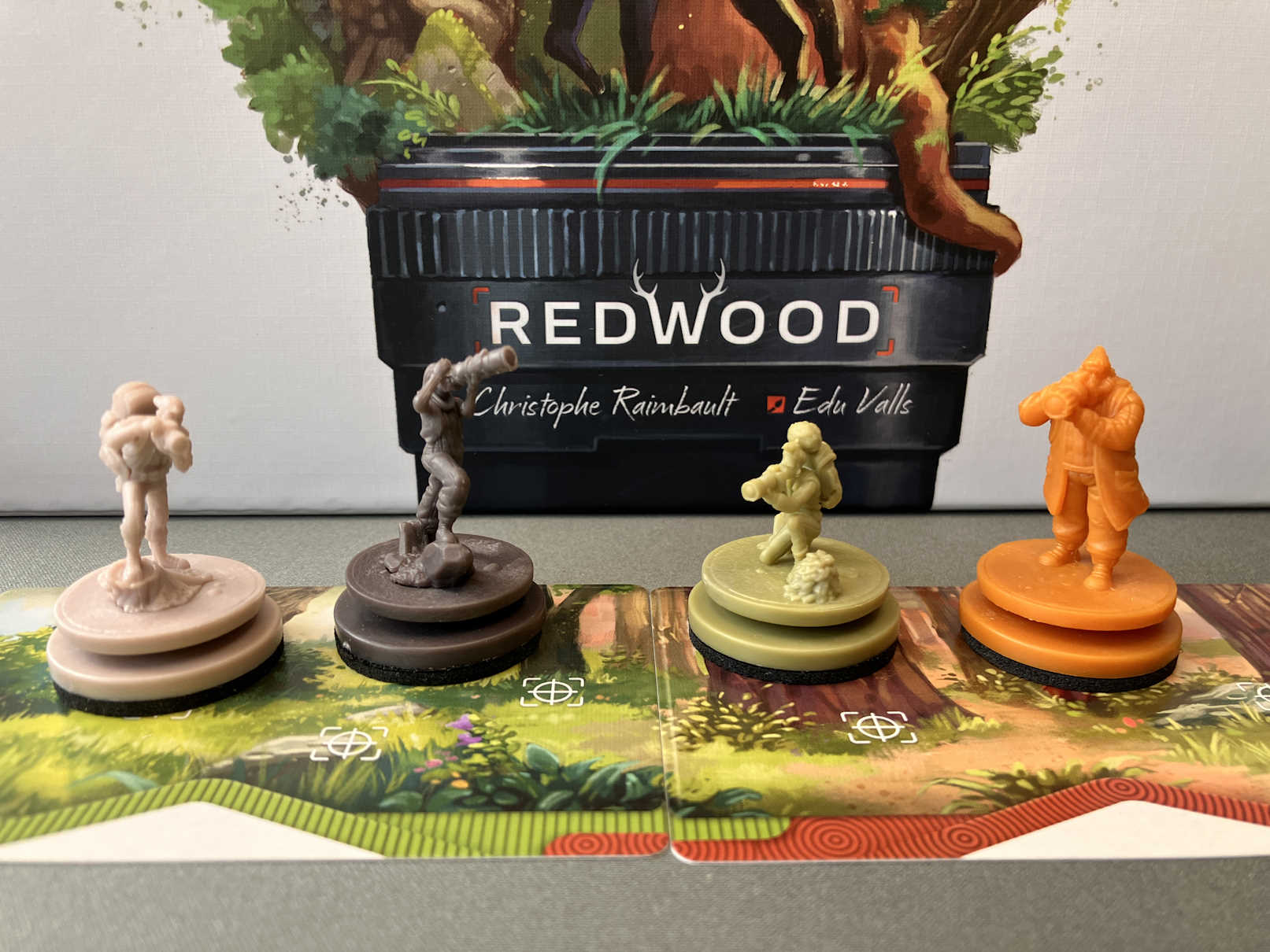 Die 4 Miniaturen in Spielerfarben stehen vor der Schachtel