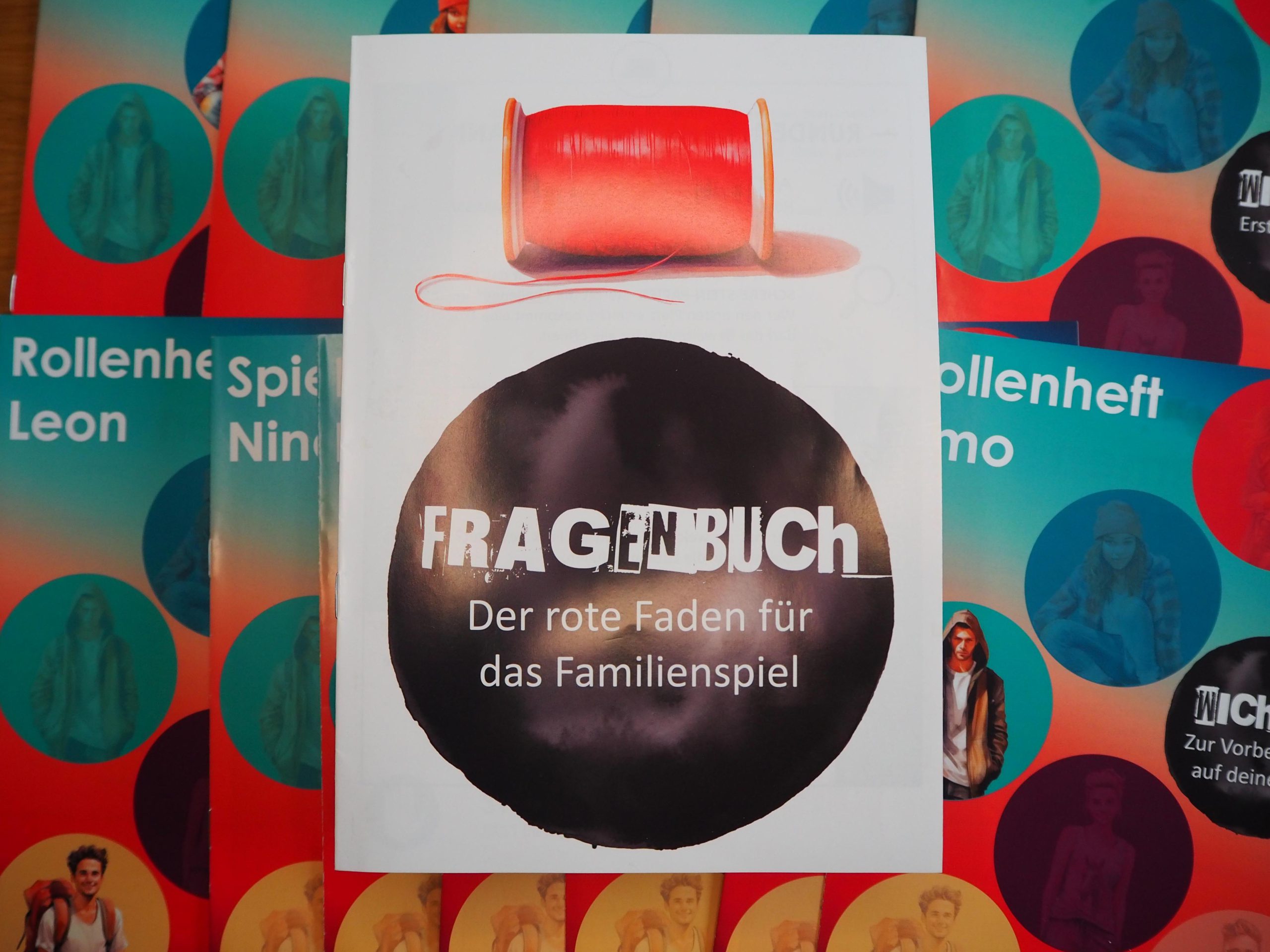 Fragenbuch im Zentrum, darunter verschiedene Rollen- und Spielhefte.