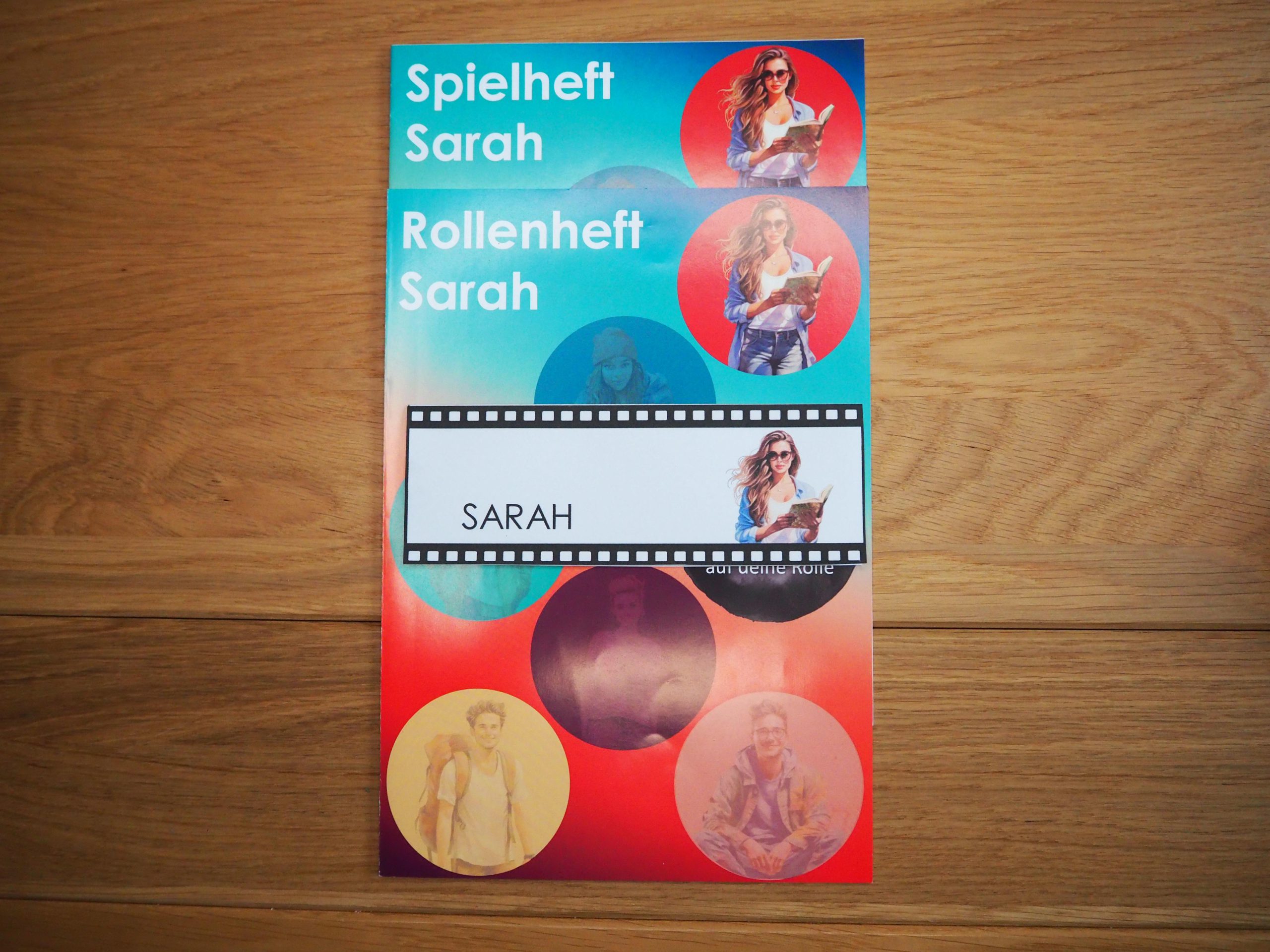 Bunte Spielhefte, Rollenhefte und ein Namensschild übereinander.
