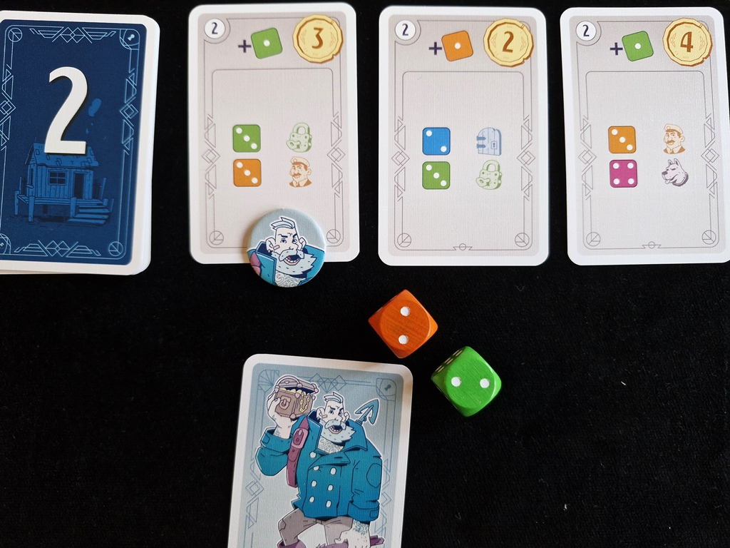 Eine der drei Zielkarten wurde markiert. Dazu liegen die passenden Würfel