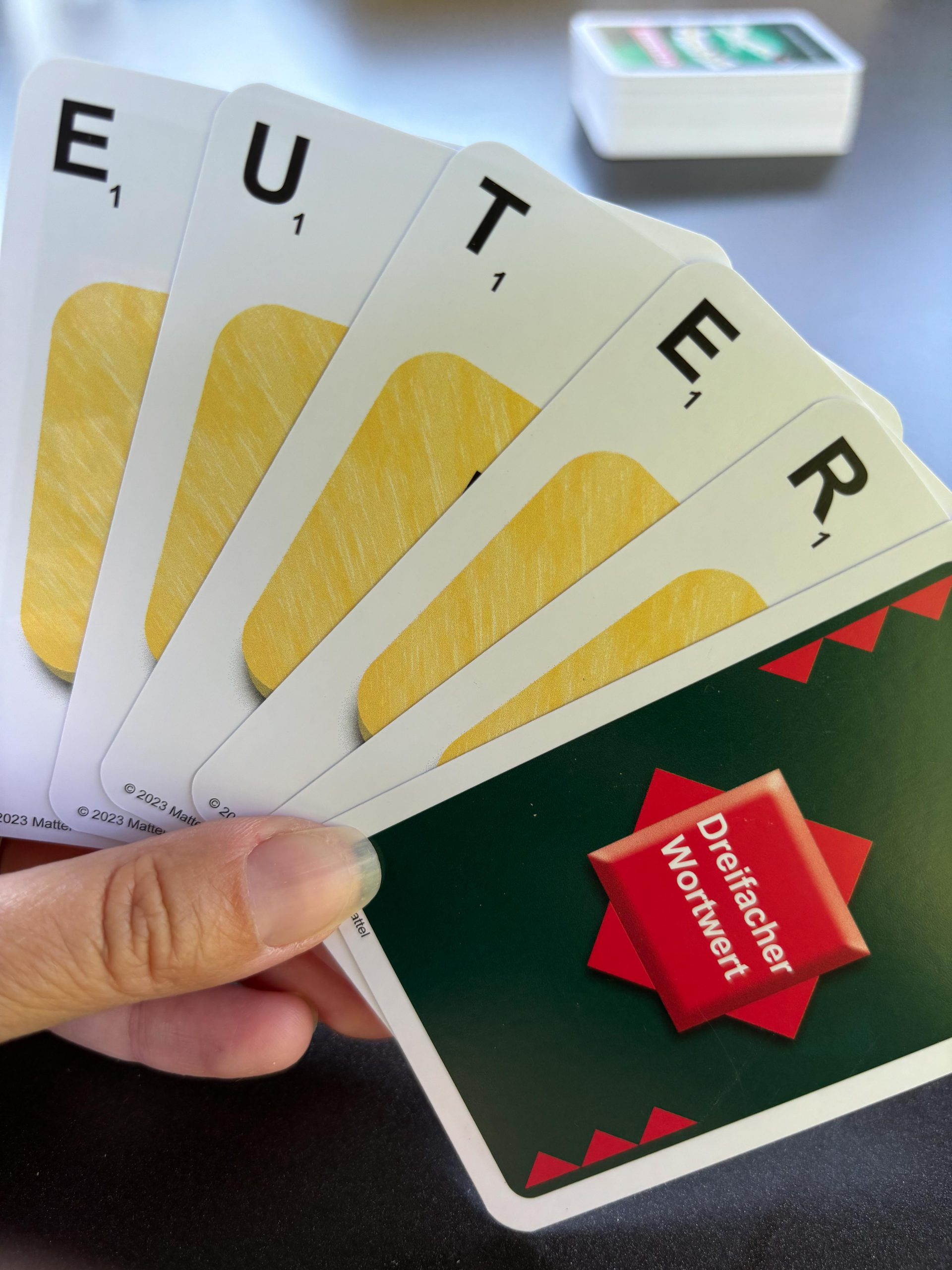 Spielkarten als Fächer in der Hand mit den Buchstaben EUTER und eine Karte dreifacher Wortwert.