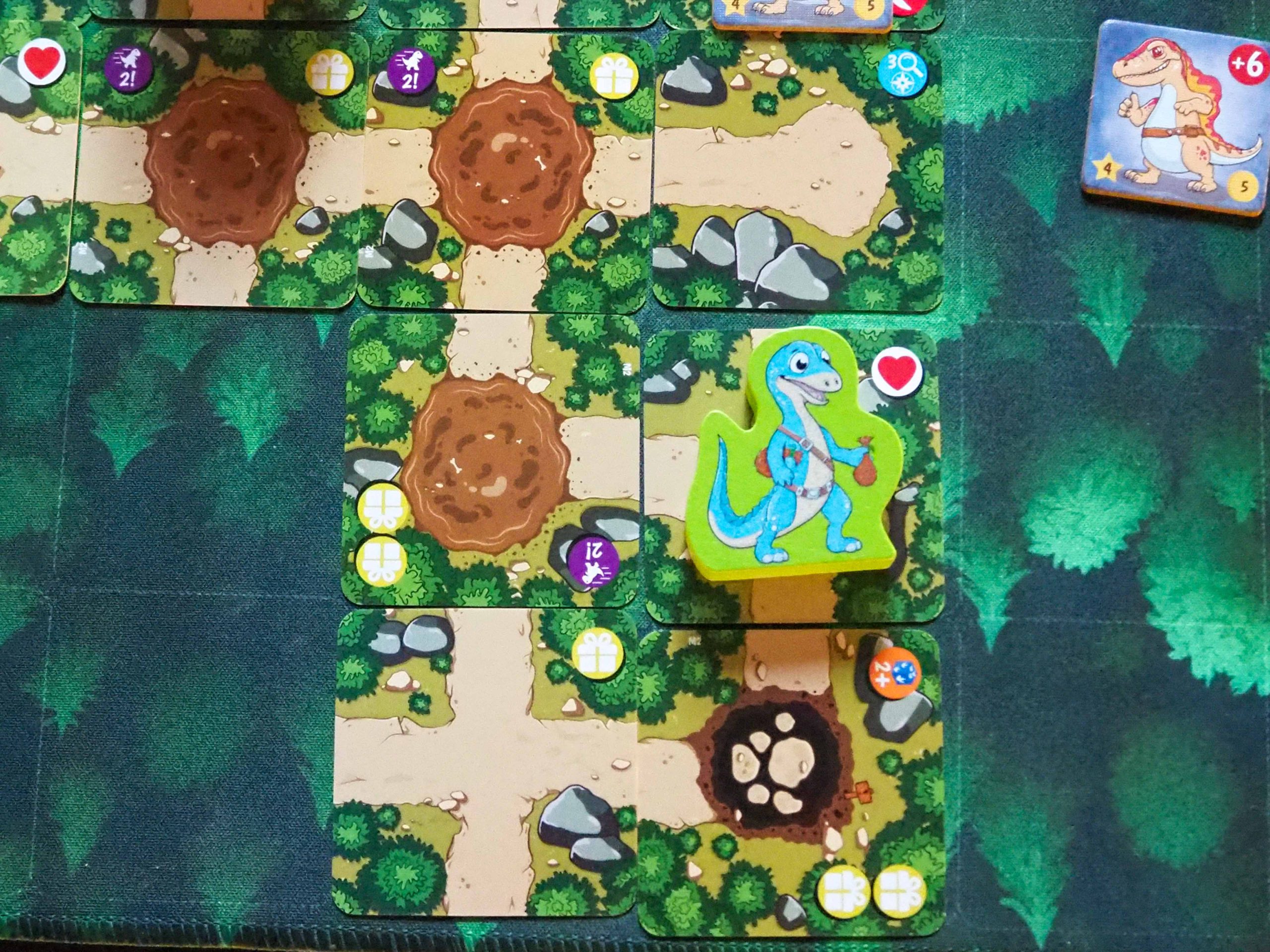 Quadratische Kacheln mit Wegen aneinander gelegt. Auf einer Kachel liegt die grüne Dino Holzfigur.